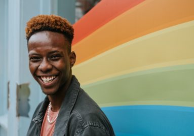 black man standing in front of rainbow mural smiling