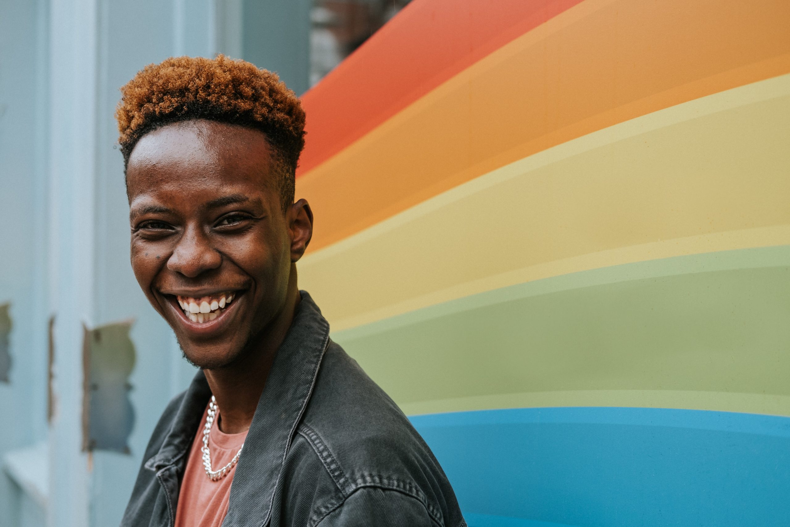 black man standing in front of rainbow mural smiling