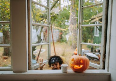 child saying boo next to halloween jackolantern perched on window