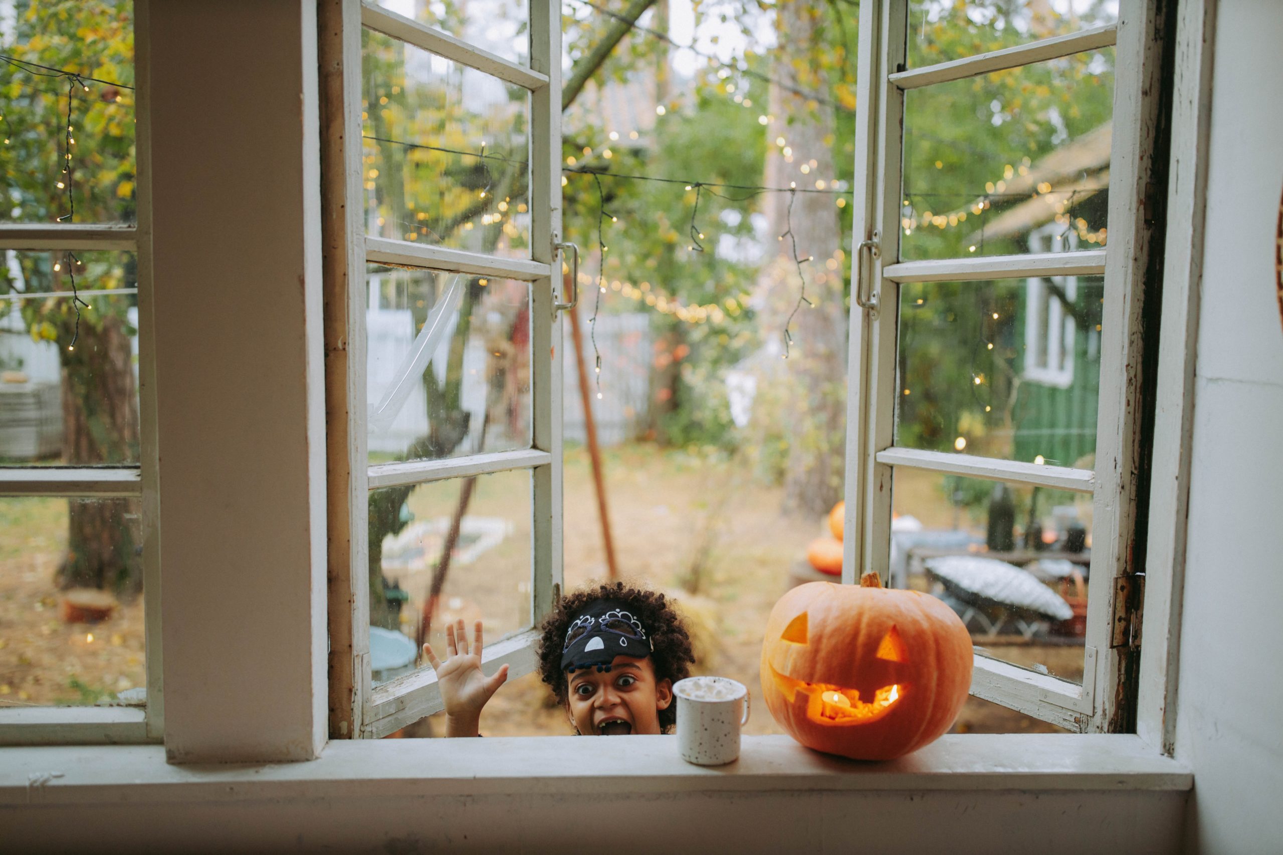 child saying boo next to halloween jackolantern perched on window
